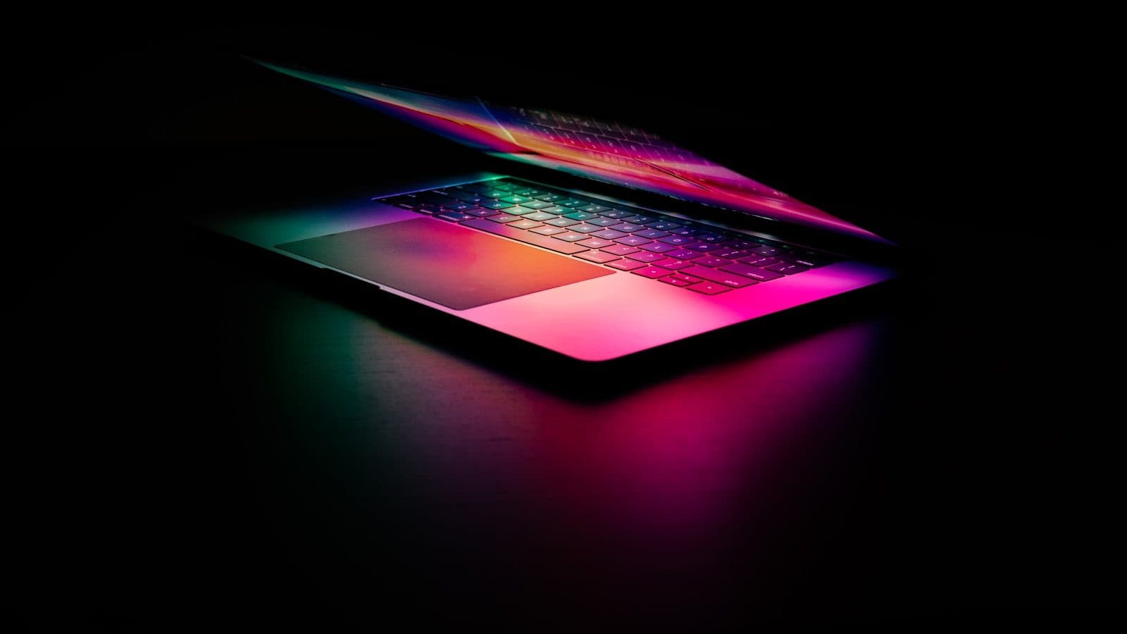 Laptop u mraku sa šarenim odsjajem osvetljene tastature